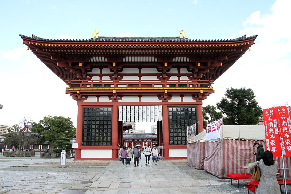 The red Gokurakumon west gate at Shitennoji Temple with visitors walking into the grounds