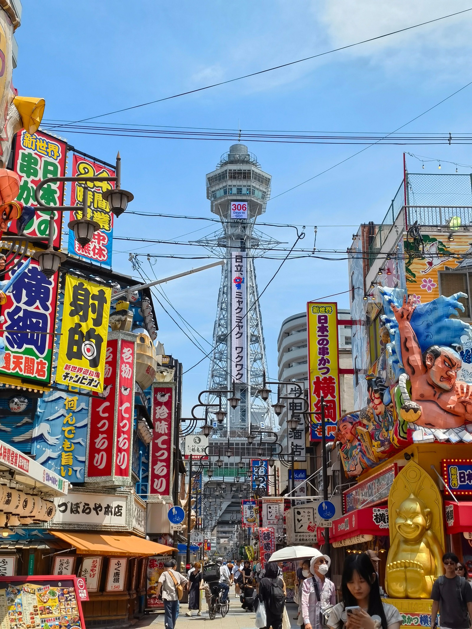 Tsutenkaku tower above colorful restaurant signs in Shinsekai on a sunny day